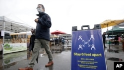 FILE - A man walks past a sign advising social distancing, at the Ferry Plaza Farmers Market, in San Francisco, California, March 28, 2020.