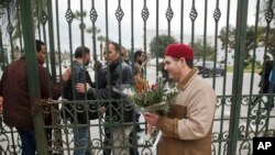 FILE - A Tunisian man hands over flowers at the entrance gate of the National Bardo Museum in Tunis, March 21, 2015. 