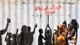 FILE - Civilians walk past graffiti reading in Arabic "Freedom, Peace, Justice and Civilian" in the Burri district of Khartoum, July 10, 2019. 