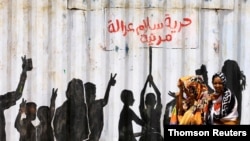 FILE - Civilians walk past graffiti reading in Arabic "Freedom, Peace, Justice and Civilian" in the Burri district of Khartoum, July 10, 2019. 