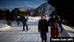 A person skiing, a mountain sport, passes by Afghan migrants Sayed Hamza, left, and Ali Rezaie as they make the crossing through the French-Italian Alps to reach a migrant center in Briançon, France on December 12, 2021. (AP Photo/Daniel Cole)