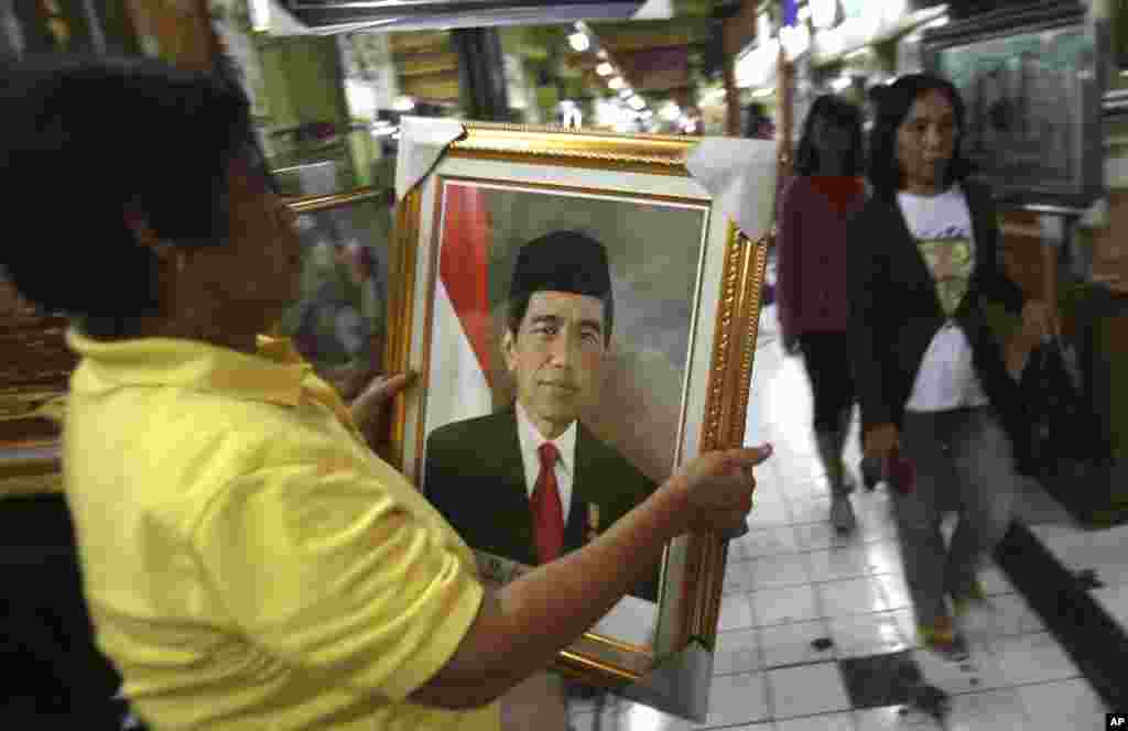 Seorang pedagang membawa potret Presiden baru Joko Widodo untuk dipasang di tokonya di Surabaya (19/10). (AP/Trisnadi)