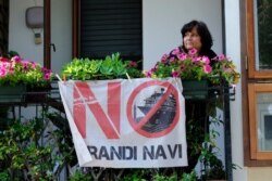 FILE - A Venetian citizen shows the flag of the movement "No grandi navi" ("No big ships") to protest against the cruise ships entering the lagoon of Venice, Italy, June 3, 2019.