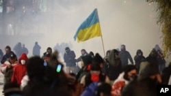 Manifestantes, uno de ellos sosteniendo la bandera nacional de Ucrania, huyen de una nube de gas lacrimógeno durante una manifestación en Tiflis, Georgia, la madrugada del lunes 2 de diciembre de 2024.