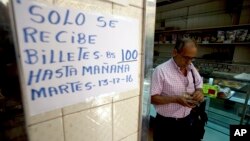 A man counts his 100-bolivar notes next to a sign alerting customers with a message in Spanish that reads: ”100-bolivar notes will only be received until Tuesday, 12-13-16,” inside a bakery in downtown Caracas, Venezuela, Dec. 12, 2016. 