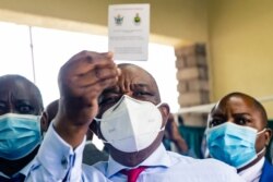 Zimbabwe vice president and Minister of Health Constantino Chiwenga holds up his vaccination certificate after receiving the first shot of Sinopharm, the COVID-19 vaccine from China, Feb. 18, 2021.