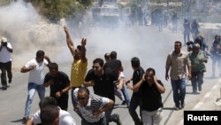 Palestinians run away from tear gas and sound grenades fired by Israeli troops during clashes following a funeral near the West Bank city of Hebron, July 23, 2015. 