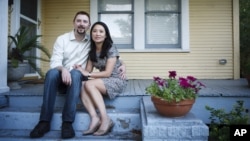 FILE - Hai Nguyen, 37 and her husband Jon Pope, 37, sit outside their home in Houston.