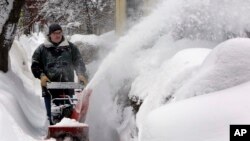 FILE - A man clears snow in Concord, N.H. Foul weather in parts of the United States has snarled transportation and slowed some business operations.