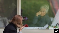 FILE - Judie Shape, right, smiles as she visits through the window and on the phone with her daughter Lori Spencer at the Life Care Center in Kirkland, Wash., near Seattle, March 17, 2020.