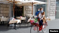 A woman wearing a protective face mask rides a bicycle past a restaurant as the outbreak of the coronavirus disease (COVID-19) continues, in Rome, Italy, Oct. 25, 2020. 