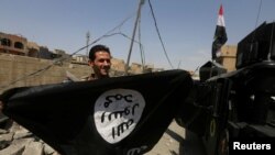 Seorang anggota unit Kontra Terorisme Irak (CTS) memperlihatkan bendera militan Islamic State saat ia merayakan kemenangan di Kota Tua Mosul, Irak, 9 Juli 2017 (foto: REUTERS/Alaa Al-Marjani)