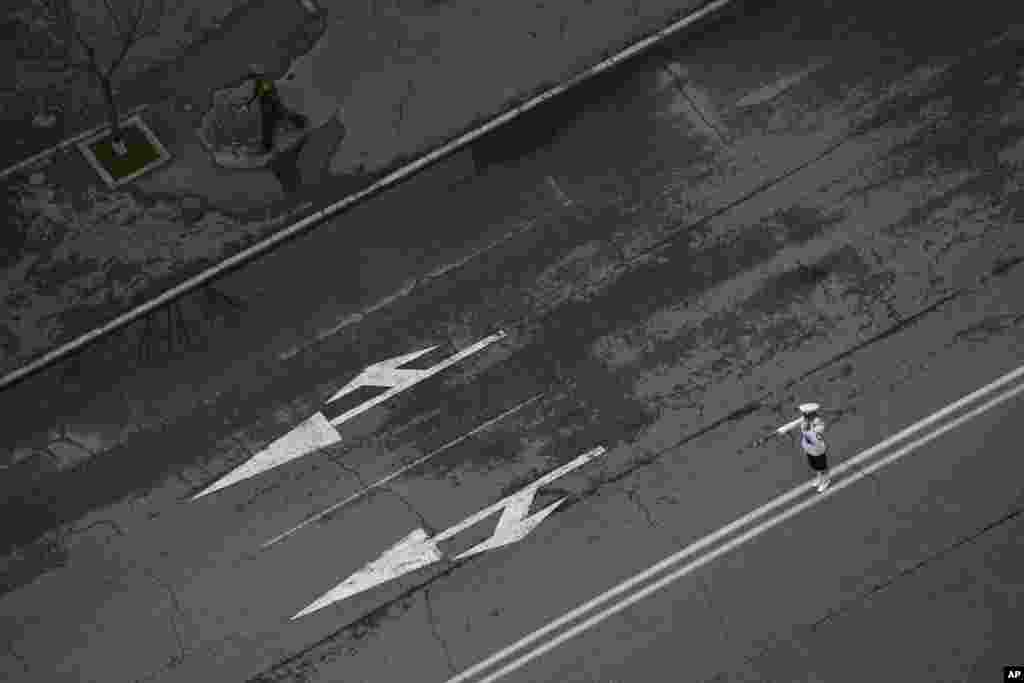 A policewoman, right bottom, directs traffic in the middle of a road while a military officer, top, walks with a traffic baton along the roadside in Pyongyang, North Korea, June 17, 2013. 