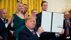 President Donald Trump holds up an executive order he signed to help combat anti-Semitism in the U. S., during a Hanukkah reception in the East Room of the White House, Dec. 11, 2019, in Washington. 