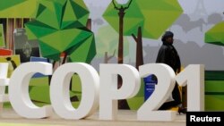 FILE - A woman walks past the COP21 logo in the Climate Generations area during the World Climate Change Conference 2015 (COP21) at Le Bourget, near Paris, France, Dec. 1, 2015. 