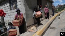 Residents wearing protective face masks hold food boxes distributed by the government during a lockdown to contain the spread of COVID-19, on the outskirts of Quito, Ecuador, May 27, 2020.