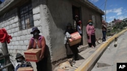 Residents wearing protective face masks hold food boxes distributed by the government during a lockdown to contain the spread of COVID-19, on the outskirts of Quito, Ecuador, May 27, 2020.