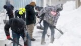 Workers clear a sidewalk of snow in Des Moines, Iowa, on January 13, 2024, as record-breaking cold continues to complicate the Iowa caucuses with snowy weather canceling many events.