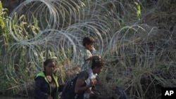 Beberapa orang migran tampak berjalan di pinggir kawat berduri yang dipasang di sepanjang tepi sungai Rio Grande di Eagle Pass, Texas, pada 1 Agustus 2023, setelah berhasil menyeberang dari Meksiko untuk menuju AS. (Foto: AP/Eric Gay)