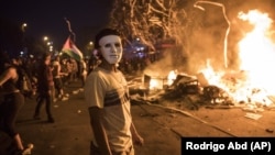 A masked anti-government protester stands by a burning barricade in Santiago, Chile, Monday, Oct. 28, 2019. 