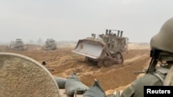 以色列军方2023年10月29日公布的有关加沙地带地面行动的视频截图显示以军装甲车在某处地点等待装甲车推土机清路。