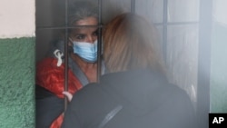 FILE - Standing behind bars, Bolivia's former president, Jeanine Anez, speaks to an unidentified woman at a police station jail, in La Paz, Bolivia, March 13, 2021. 