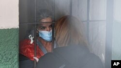 FILE - Standing behind bars, Bolivia's former president, Jeanine Anez, speaks to an unidentified woman at a police station jail, in La Paz, Bolivia, March 13, 2021. 