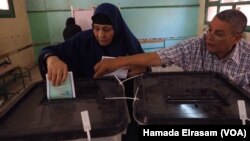 A polling station employee helps a female voter place her ballot in the correct box during parliamentary elections in Giza, Egypt, Oct. 18, 2015.