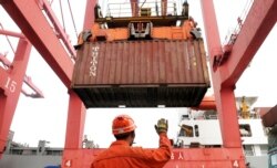 FILE - An employee guides as a crane unloads shipping containers from a cargo ship at a port in Lianyungang, Jiangsu province, China, March 8, 2014.