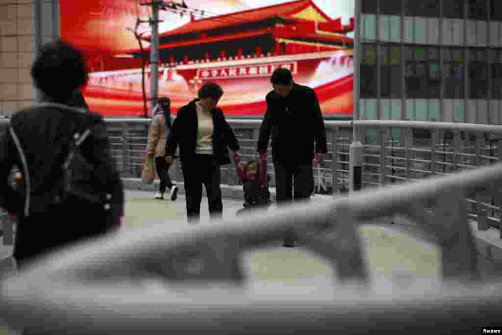 A family walks in front of a screen showing propaganda displays on a bridge in Shanghai, China, November 8, 2012.