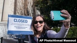 Jamie Parrish of Minneapolis takes a selfie in front of the closed sign at the National Archives, Dec. 22, 2018, in Washington. Congress' inability to approve a funding measure that includes money for a proposed U.S.-Mexico border wall has led to a partial government shutdown.