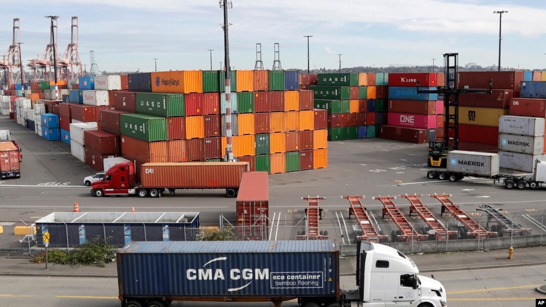 FILE - Trucks hauling shipping containers drive near containers stacked five-high at a terminal on Harbor Island in Seattle, Oct. 2, 2019.