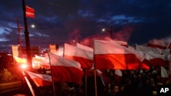 FILE - Demonstrators burn flares and wave Polish flags during an annual march to mark Poland's National Independence Day, in Warsaw, Poland, Nov. 11, 2017. 