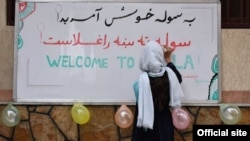 A girl writes on a sign welcoming people to the School of Leadership, Afghanistan (SOLA) in Kabul. (Source - Official site)