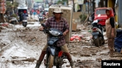 Man carrying a washing machine rides a motorbike as he collects items at a residential area affected by floods in Bekasi, West Java province, Indonesia, Jan. 3, 2020.