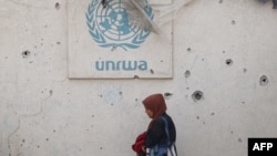 Palestinka prolazi pored oštećenog zida s logotipom UNRWA-e u kampu za interno raseljene osobe u Rafahu u južnom Pojasu Gaze 28. maja 2024.