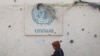 FILE - Seorang perempuan Palestina berjalan melewati tembok yang rusak dengan logo UNRWA di kamp pengungsi di Rafah, Jalur Gaza selatan, 28 Mei 2024, di tengah konflik Israel-Hamas. (Eyad BABA / AFP)