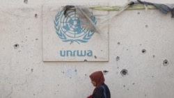 FILE - Seorang perempuan Palestina berjalan melewati tembok yang rusak dengan logo UNRWA di kamp pengungsi di Rafah, Jalur Gaza selatan, 28 Mei 2024, di tengah konflik Israel-Hamas. (Eyad BABA / AFP)