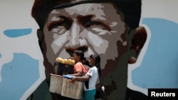 Women walk past a portrait of Venezuela's late President Hugo Chavez in Caracas, Venezuela August 7, 2017. 