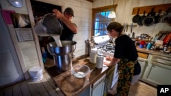 FILE - Phil Retberg empties a bucket of raw milk that will be bottled by his wife, Heather, right, at their farm, Sept. 17, 2021, in Penobscot, Maine. 