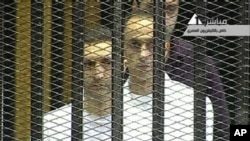 This video image taken from Egyptian State Television shows the sons of Hosni Mubarak, Alaa Mubarak, left and Gamal Mubarak as they stand inside the cage of mesh and iron bars in a Cairo courtroom Wednesday Aug. 3, 2011 as his historic trial began on c