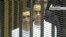 This video image taken from Egyptian State Television shows the sons of Hosni Mubarak, Alaa Mubarak, left and Gamal Mubarak as they stand inside the cage of mesh and iron bars in a Cairo courtroom Wednesday Aug. 3, 2011 as his historic trial began on c
