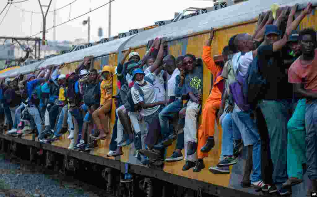 Train commuters hold on to the side of an overcrowded passenger train in Soweto, South Africa.