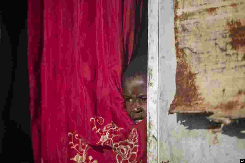 Jonelson Princeton, 7, who survived cholera as a newborn, peers out from inside his home which was once used as an office, on a former UN base where he lives with his parents and grandmother in Mirebalais, Haiti, Monday, Oct. 19, 2020. Ten years after a c