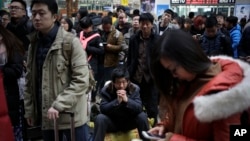 A man, center, sits on his belonging as he waits with other Chinese traveler to board a at the south train station in Beijing, Jan. 31, 2016.