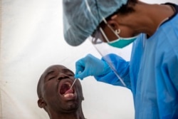 A man opens his mouth as a heath worker tests for the coronavirus during a campaign aimed to combat the spread of COVID-19 in Diepsloot, north Johannesburg, South Africa, Friday, May 8, 2020. (AP Photo)