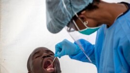 A man opens his mouth as a heath worker tests for the coronavirus during a campaign aimed to combat the spread of COVID-19 in Diepsloot, north Johannesburg, South Africa, Friday, May 8, 2020. (AP Photo)