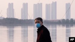 FILE - In this Jan. 30, 2020 file photo, a man wears a face mask as he stands along the waterfront in Wuhan in central China's Hubei Province.