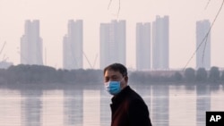 FILE - In this Jan. 30, 2020 file photo, a man wears a face mask as he stands along the waterfront in Wuhan in central China's Hubei Province.