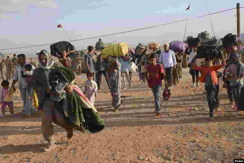 Syrian Kurds walk with their belongings after crossing into Turkey at the Turkish-Syrian border, near the southeastern town of Suruc in Sanliurfa province, September 20, 2014. About 60,000 Syrian Kurds fled into Turkey in the space of 24 hours, a deputy p
